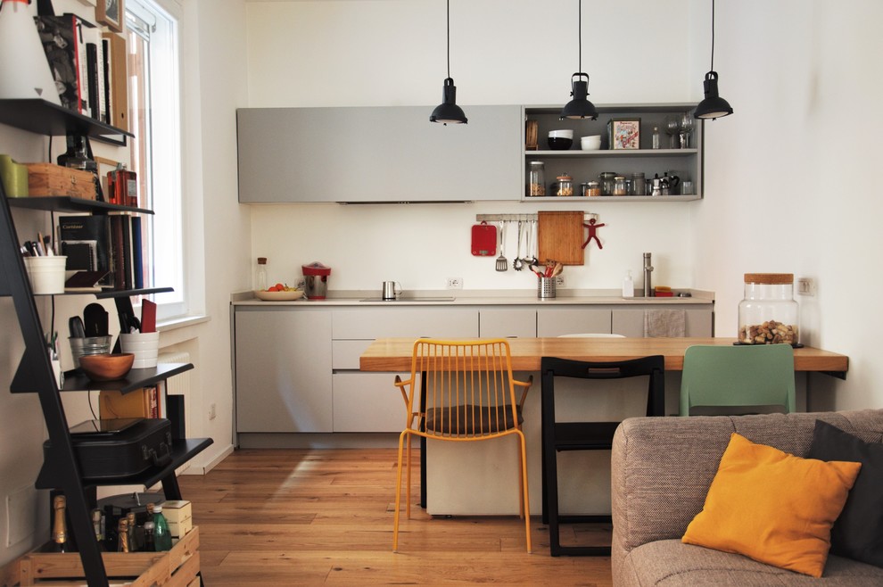 Diseño de cocina lineal contemporánea abierta sin isla con puertas de armario grises, suelo de madera clara, armarios con paneles lisos y suelo marrón