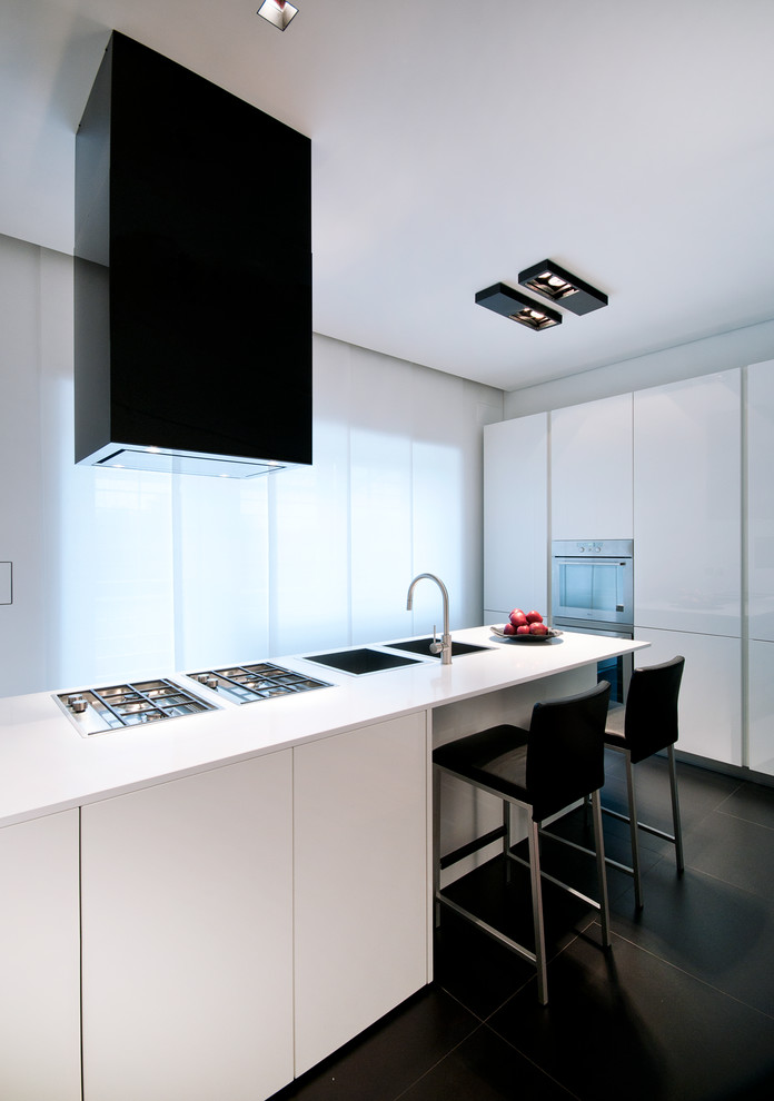 Imagen de cocina contemporánea con fregadero de doble seno, armarios con paneles lisos, puertas de armario blancas, una isla, suelo negro y encimeras blancas
