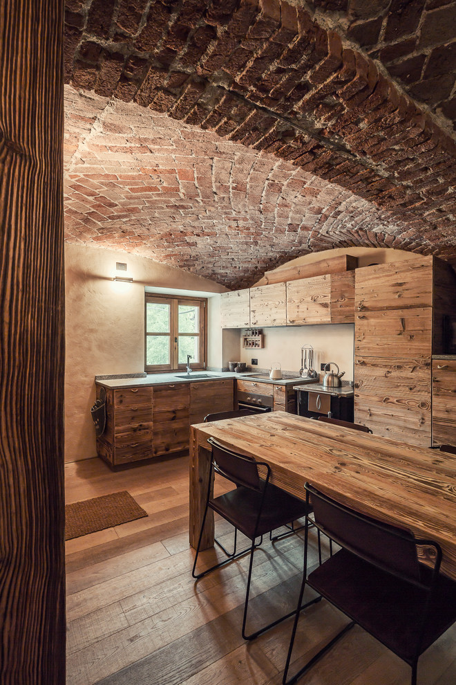 Mittelgroße Rustikale Wohnküche ohne Insel in L-Form mit flächenbündigen Schrankfronten, hellbraunen Holzschränken, Küchenrückwand in Beige, braunem Holzboden, braunem Boden und Küchengeräten aus Edelstahl in Turin