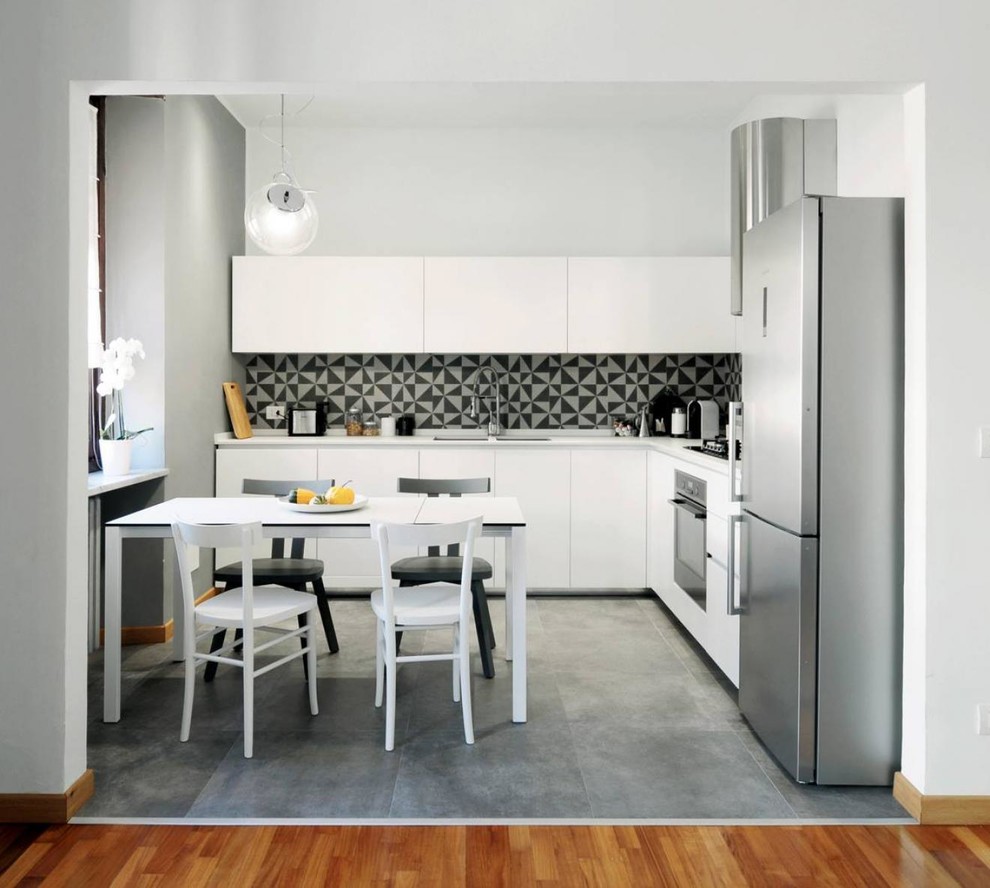 Пример оригинального дизайна: угловая кухня-гостиная в стиле модернизм с белыми фасадами, разноцветным фартуком и серым полом без острова