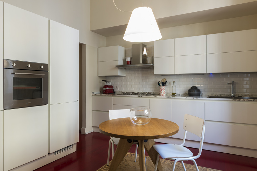 Example of a mid-sized trendy single-wall light wood floor and red floor enclosed kitchen design in Milan with a double-bowl sink, flat-panel cabinets, white cabinets, marble countertops, white backsplash, subway tile backsplash, stainless steel appliances and no island
