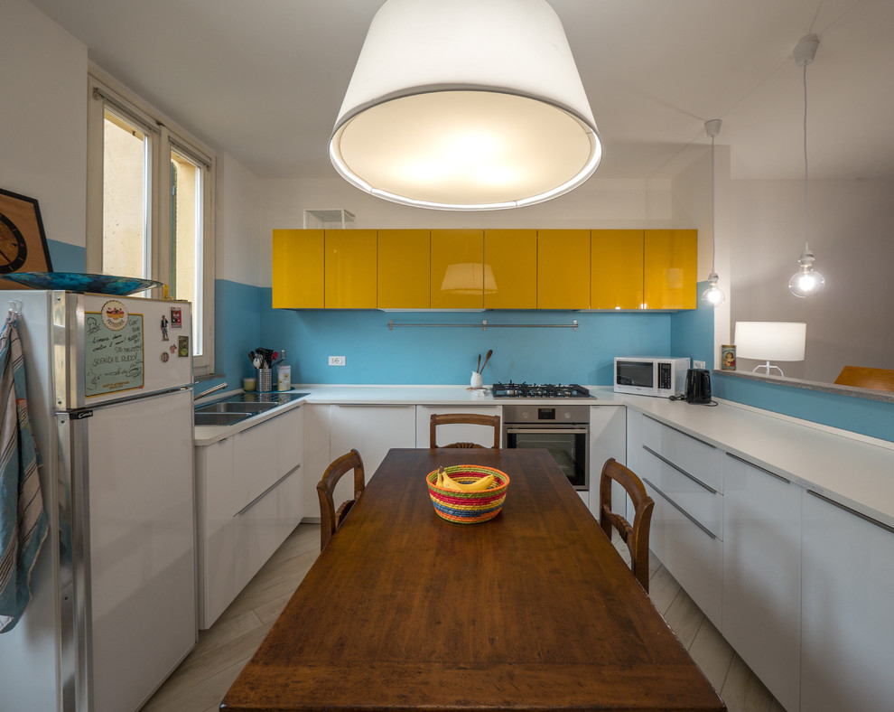 Пример оригинального дизайна: п-образная кухня-гостиная среднего размера в стиле фьюжн с двойной мойкой, плоскими фасадами, желтыми фасадами, столешницей из ламината, синим фартуком и белой техникой без острова