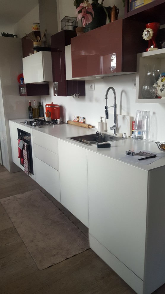 Foto di una piccola cucina minimalista con lavello da incasso, ante di vetro, ante rosse, top in vetro, paraspruzzi bianco, elettrodomestici in acciaio inossidabile e nessuna isola