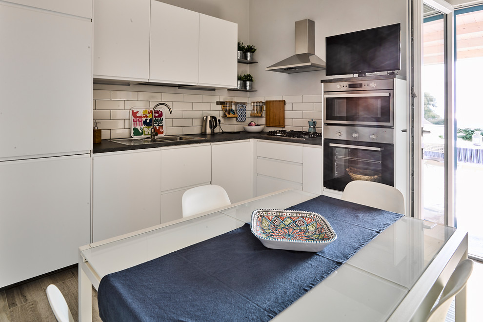 Example of a small trendy l-shaped ceramic tile eat-in kitchen design in Other with a single-bowl sink, flat-panel cabinets, white cabinets, white backsplash, ceramic backsplash, stainless steel appliances and no island