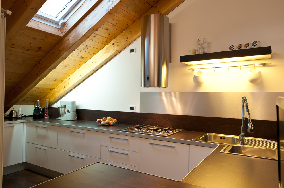 Modern inredning av ett avskilt, litet l-kök, med en nedsänkt diskho, vita skåp, laminatbänkskiva, grått stänkskydd, rostfria vitvaror, klinkergolv i porslin och en halv köksö