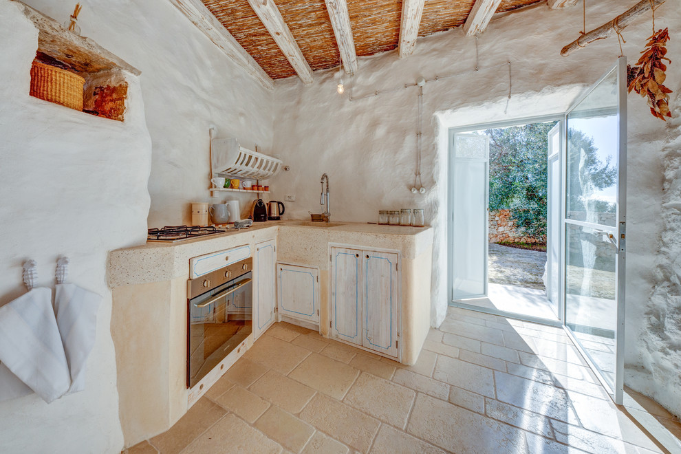 Immagine di una cucina a L mediterranea di medie dimensioni con lavello a vasca singola, ante con finitura invecchiata, paraspruzzi bianco, elettrodomestici in acciaio inossidabile, pavimento beige e top beige