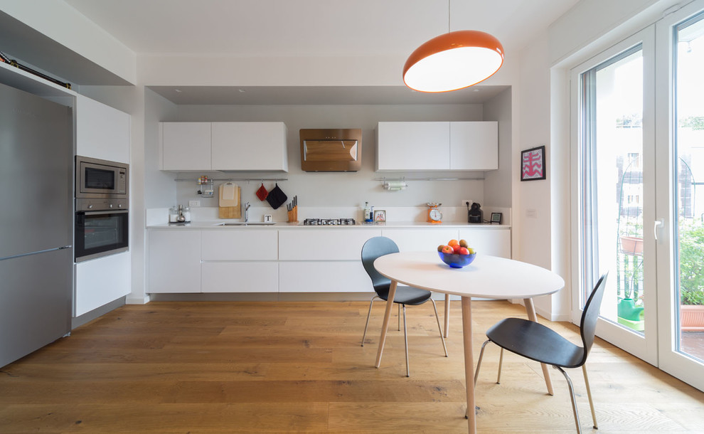 Bild på ett mellanstort minimalistiskt linjärt kök och matrum, med släta luckor, vita skåp, vitt stänkskydd, rostfria vitvaror, mellanmörkt trägolv, brunt golv och en undermonterad diskho