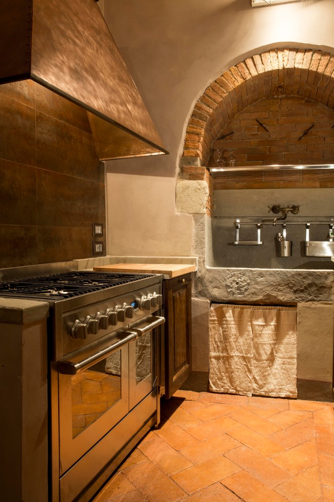 フィレンツェにある低価格の小さな地中海スタイルのおしゃれなキッチン (エプロンフロントシンク、レイズドパネル扉のキャビネット、中間色木目調キャビネット、大理石カウンター、シルバーの調理設備、レンガの床) の写真