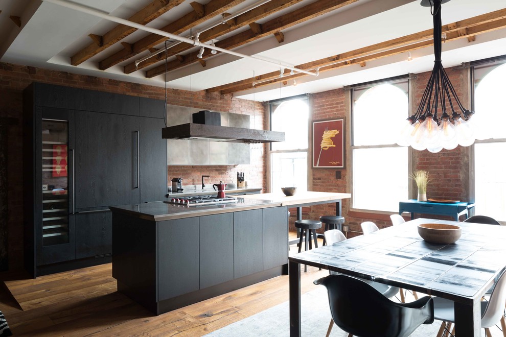 Foto på ett industriellt kök, med släta luckor, svarta skåp, integrerade vitvaror, mellanmörkt trägolv, en köksö och brunt golv