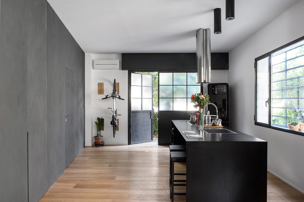 Idéer för att renovera ett mellanstort industriellt svart svart kök, med en enkel diskho, svarta vitvaror, ljust trägolv, en köksö och beiget golv