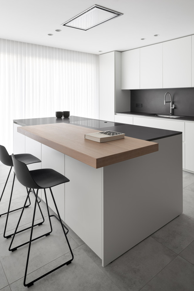 Medium sized contemporary galley kitchen in Venice with a submerged sink, flat-panel cabinets, white cabinets, black splashback, an island, grey floors and black worktops.