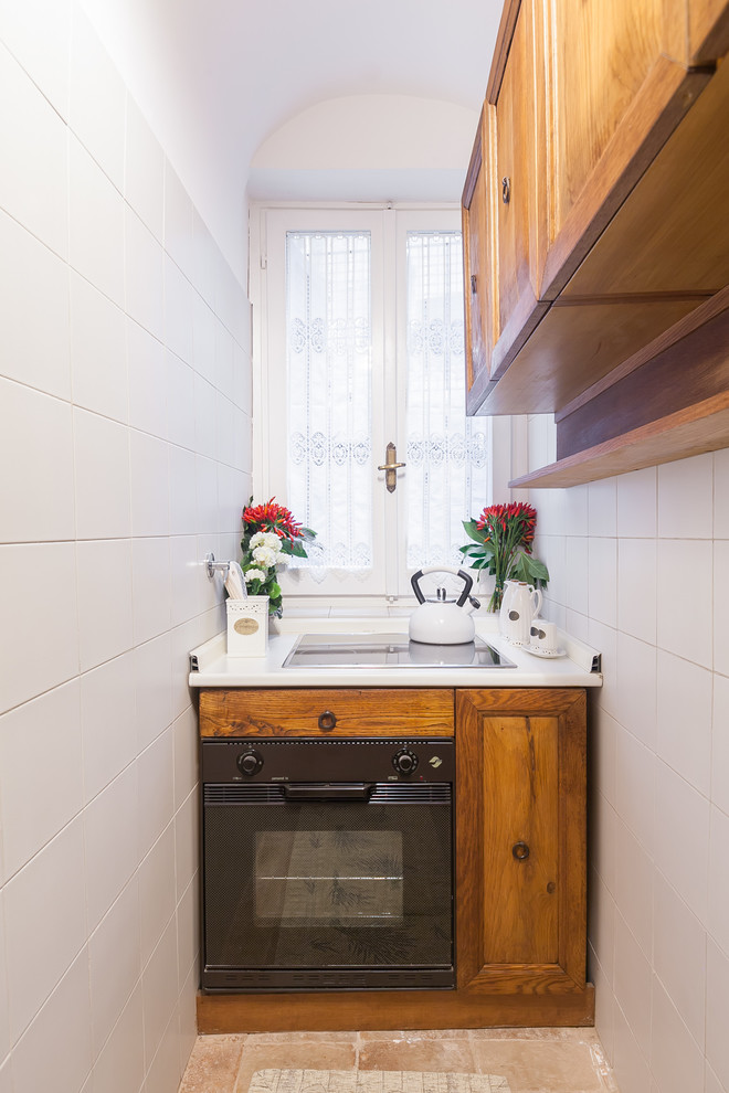 Cette photo montre une petite cuisine nature en bois brun avec un placard avec porte à panneau encastré, un plan de travail en surface solide, un électroménager noir et un sol en brique.