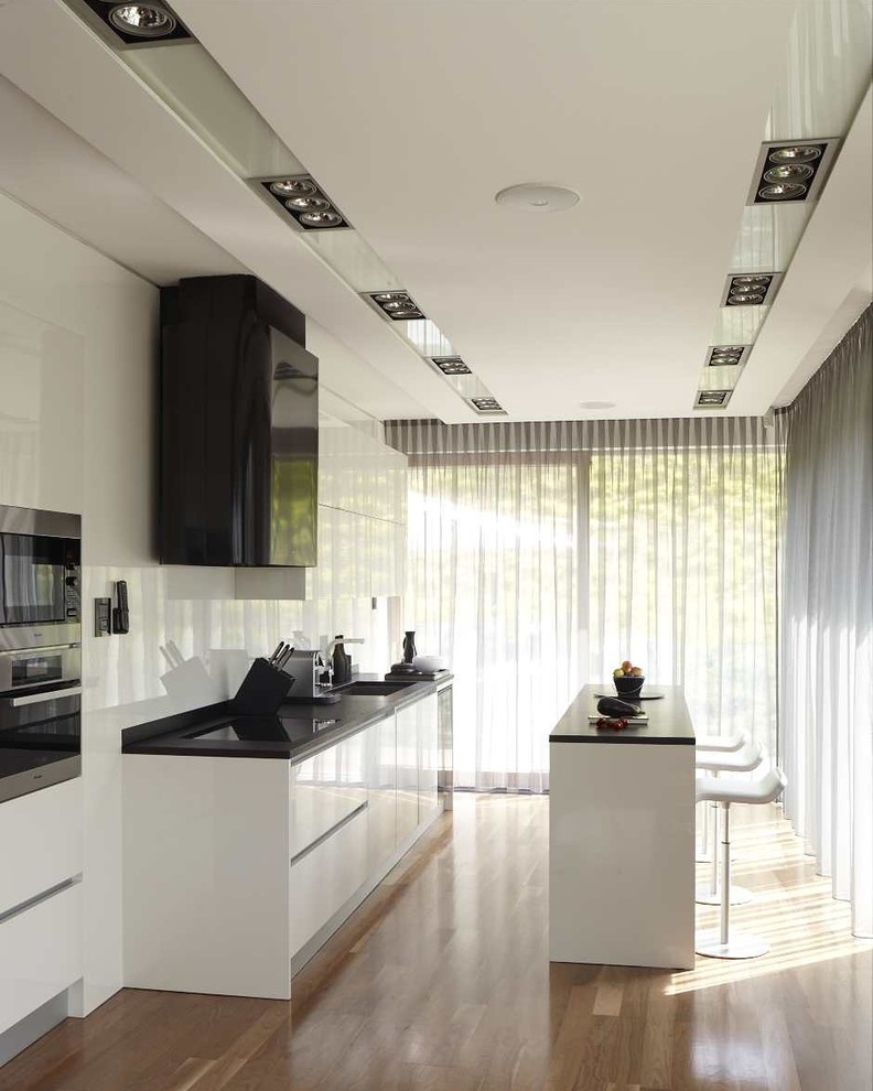 Moderne Küche mit Waschbecken, flächenbündigen Schrankfronten, Kücheninsel, schwarzer Arbeitsplatte und braunem Holzboden in Sonstige