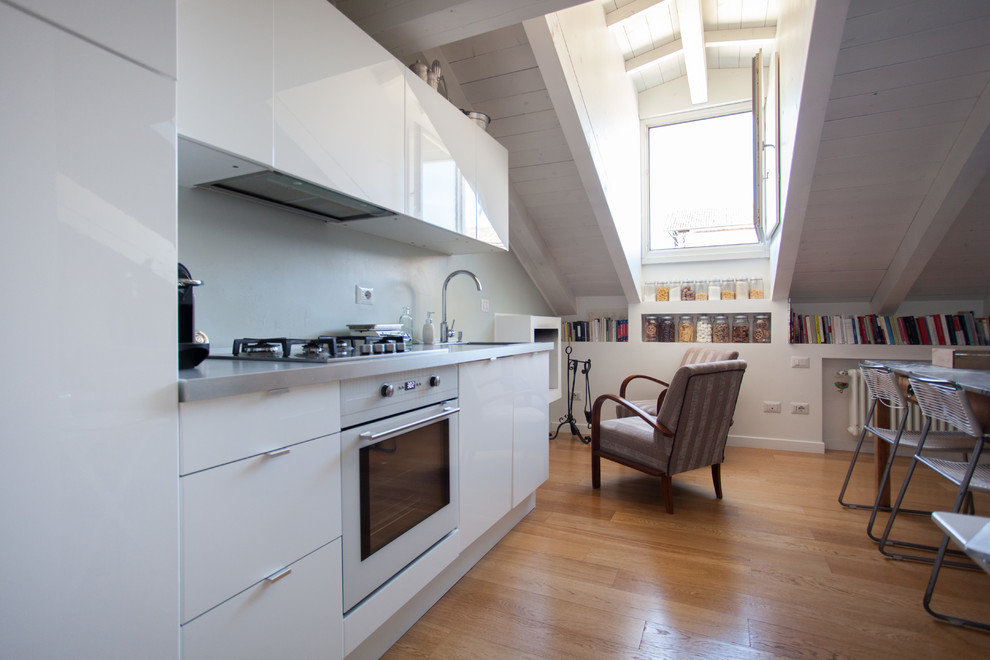 Immagine di una piccola cucina minimal con ante bianche, top in acciaio inossidabile, pavimento in legno massello medio, nessuna isola e ante lisce