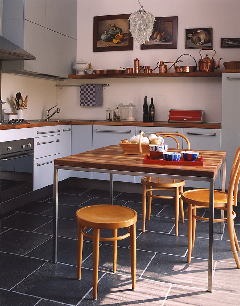 Lantlig inredning av ett mellanstort kök, med släta luckor, vita skåp, träbänkskiva, vitt stänkskydd, rostfria vitvaror och svart golv