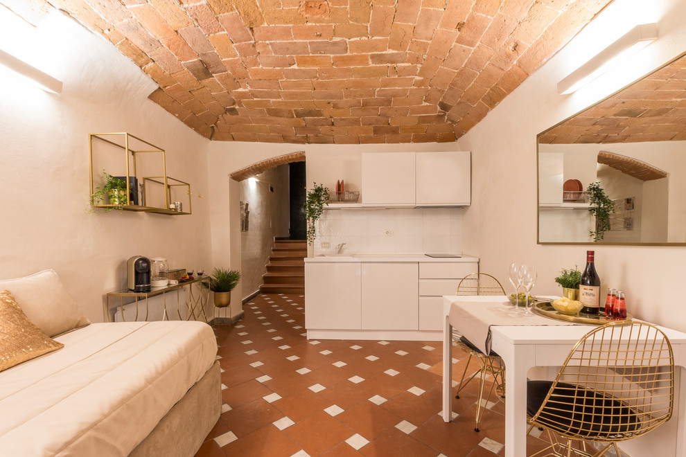 フィレンツェにある小さな地中海スタイルのおしゃれなキッチン (ドロップインシンク、フラットパネル扉のキャビネット、白いキャビネット、白いキッチンパネル、アイランドなし、茶色い床、白いキッチンカウンター) の写真