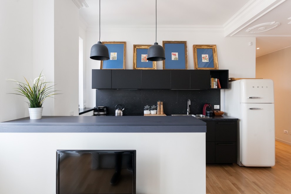 Foto di una cucina parallela moderna con ante lisce, paraspruzzi nero, penisola, top nero, lavello da incasso, elettrodomestici bianchi e parquet chiaro