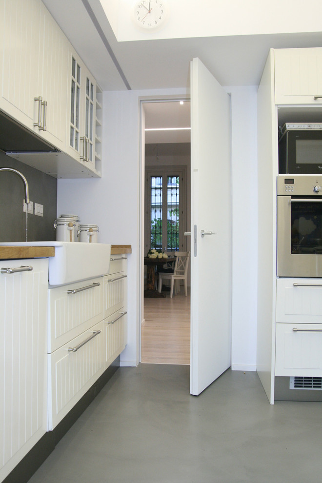 Idee per una cucina shabby-chic style di medie dimensioni con lavello da incasso, ante con bugna sagomata, ante bianche, top in legno, paraspruzzi grigio e pavimento in cemento