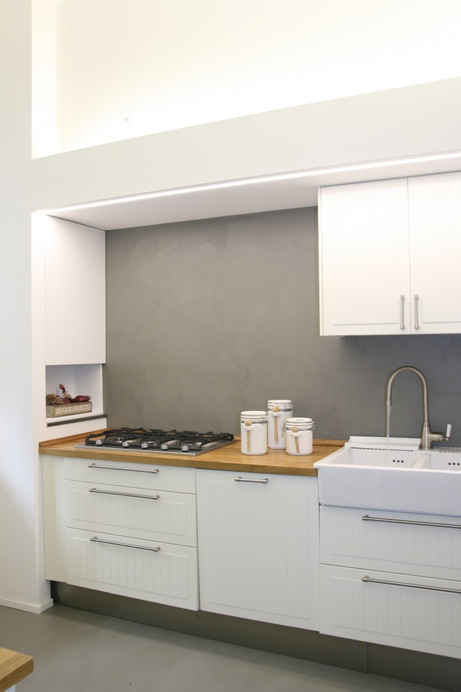 Bild på ett mellanstort shabby chic-inspirerat kök, med en nedsänkt diskho, luckor med upphöjd panel, vita skåp, träbänkskiva, grått stänkskydd och betonggolv