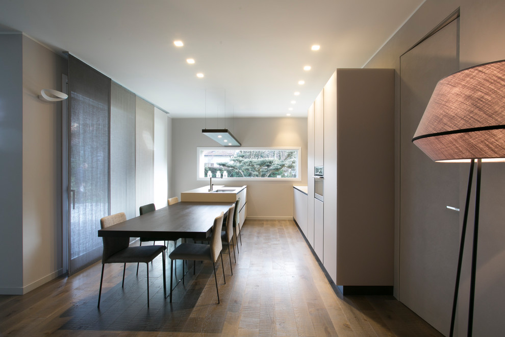 Modelo de cocina lineal minimalista grande abierta con fregadero bajoencimera, armarios tipo vitrina, encimera de azulejos, electrodomésticos de acero inoxidable, suelo de madera oscura y una isla