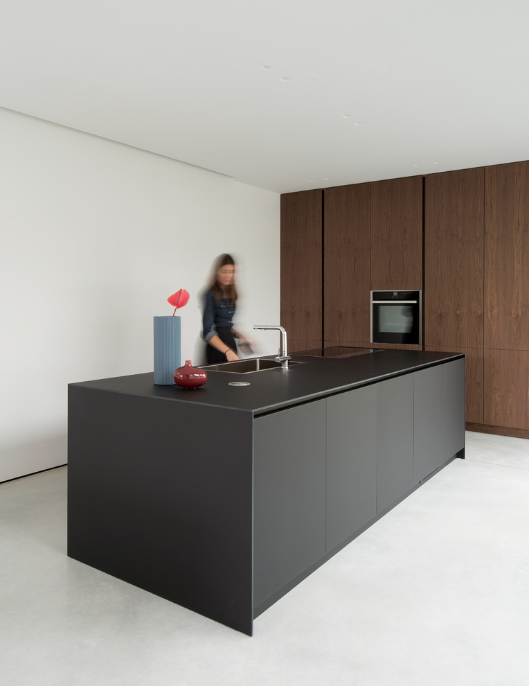 Imagen de cocina moderna con fregadero de un seno, armarios con paneles lisos, puertas de armario de madera en tonos medios, electrodomésticos negros, una isla, suelo gris y encimeras negras