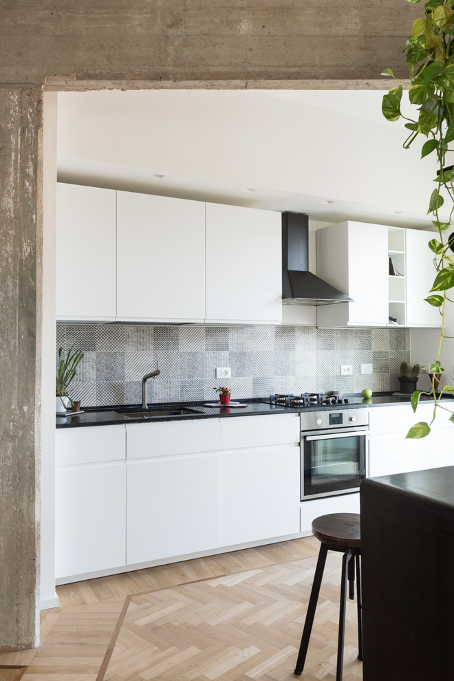 This is an example of a contemporary kitchen in Rome with a submerged sink, white cabinets, granite worktops, yellow splashback, porcelain splashback, light hardwood flooring, brown floors and black worktops.