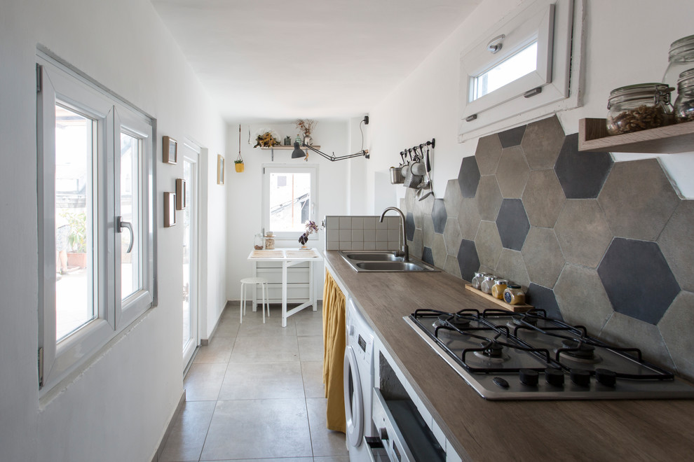 Inredning av ett nordiskt avskilt, litet brun linjärt brunt kök, med en dubbel diskho, öppna hyllor, vita skåp, träbänkskiva, flerfärgad stänkskydd, stänkskydd i cementkakel, rostfria vitvaror, klinkergolv i porslin och grått golv