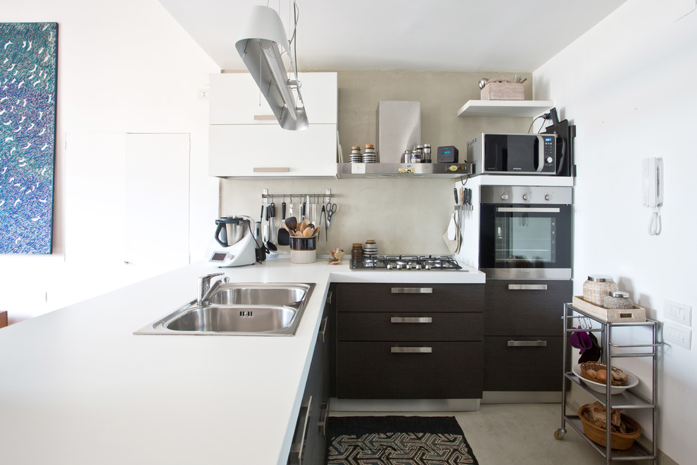 Immagine di una piccola cucina eclettica con lavello a doppia vasca, ante grigie, paraspruzzi grigio, pavimento in cemento, penisola, pavimento grigio e top bianco