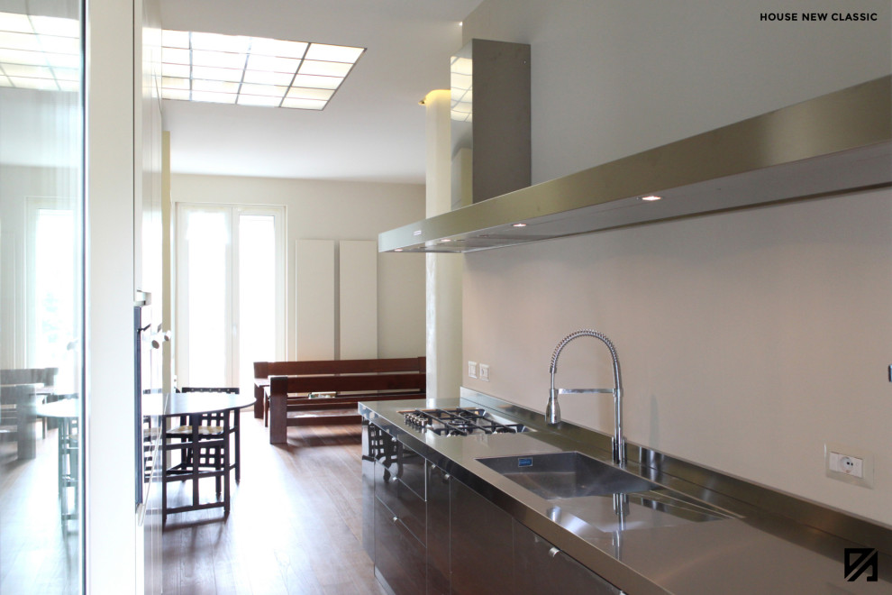 Foto på ett litet funkis linjärt kök och matrum, med en integrerad diskho, skåp i rostfritt stål, bänkskiva i rostfritt stål, rostfria vitvaror, mellanmörkt trägolv och rött golv
