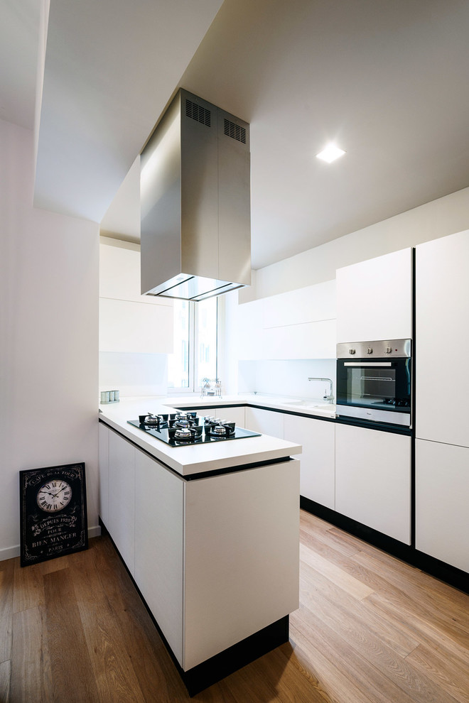 Small contemporary u-shaped open plan kitchen in Rome with flat-panel cabinets, white cabinets, stainless steel appliances, light hardwood flooring and a breakfast bar.