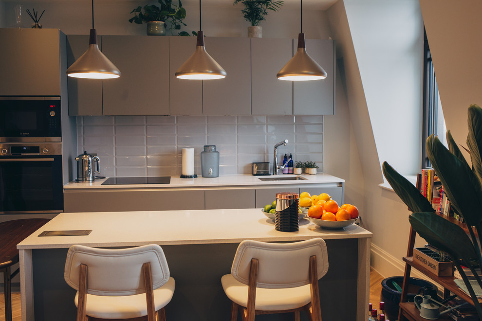Bild på ett litet funkis vit linjärt vitt kök och matrum, med en enkel diskho, släta luckor, grå skåp, laminatbänkskiva, rostfria vitvaror, ljust trägolv, en köksö och brunt golv