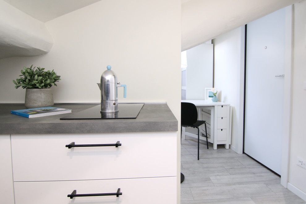This is an example of a small contemporary galley open plan kitchen in Milan with a built-in sink, flat-panel cabinets, white cabinets, laminate countertops, white splashback, black appliances, porcelain flooring, no island, grey floors and grey worktops.