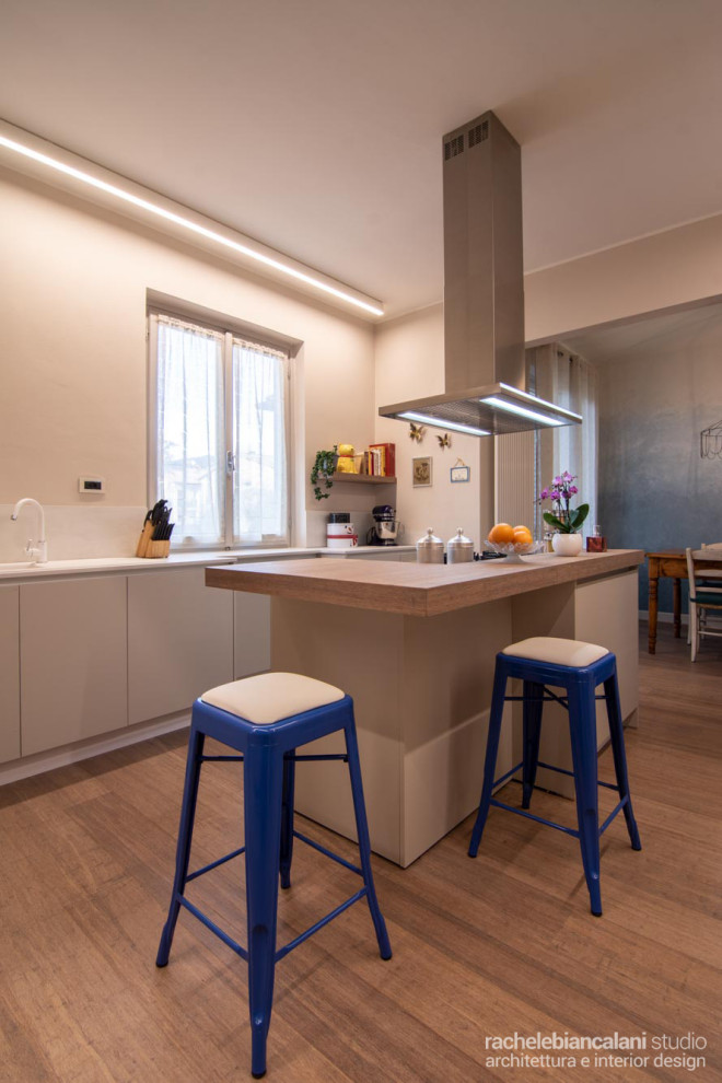 Inspiration for a large modern galley open plan kitchen in Florence with a built-in sink, flat-panel cabinets, beige cabinets, quartz worktops, white splashback, engineered quartz splashback, stainless steel appliances, bamboo flooring, an island, brown floors and white worktops.