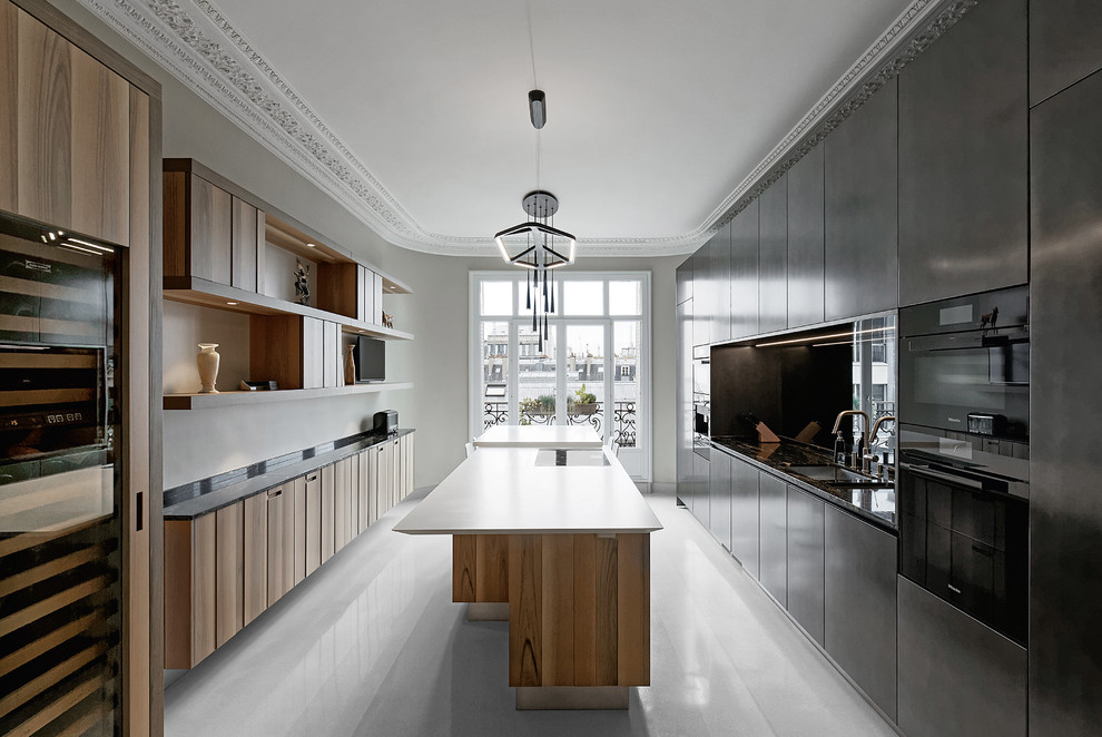 Cette image montre une grande cuisine parallèle design fermée avec un placard à porte plane, des portes de placard noires, un électroménager noir, îlot et un sol blanc.
