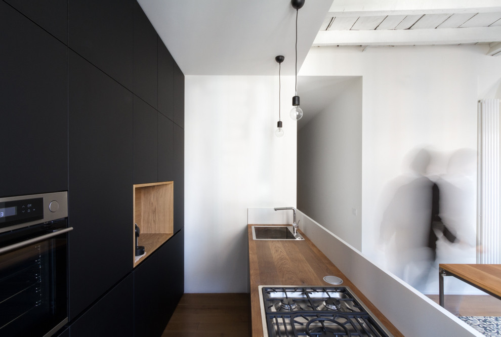 Mittelgroße, Zweizeilige Moderne Küche mit Einbauwaschbecken, flächenbündigen Schrankfronten, schwarzen Schränken, Küchengeräten aus Edelstahl und dunklem Holzboden in Mailand