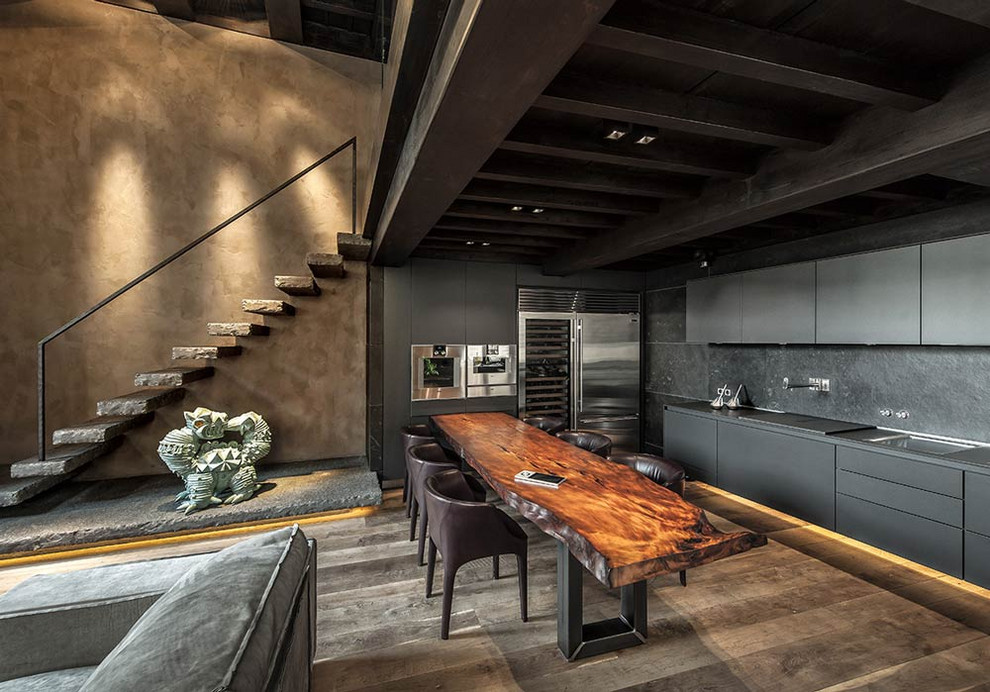 フィレンツェにあるインダストリアルスタイルのおしゃれなLDK (フラットパネル扉のキャビネット、黒いキャビネット、黒いキッチンパネル、シルバーの調理設備、茶色い床、黒いキッチンカウンター) の写真
