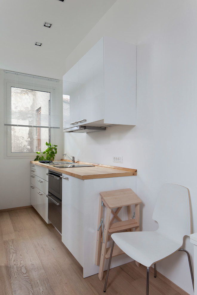 Esempio di una piccola cucina scandinava con lavello da incasso, ante lisce, ante bianche, top in legno, paraspruzzi bianco, elettrodomestici neri, pavimento in legno massello medio e nessuna isola