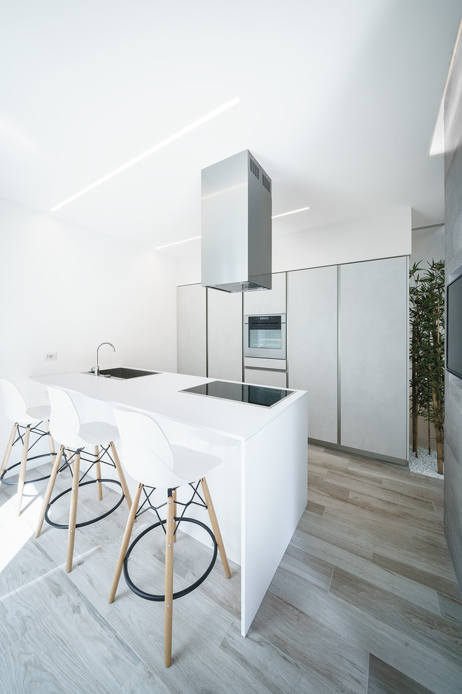 Moderne Küche mit flächenbündigen Schrankfronten, Küchengeräten aus Edelstahl, Halbinsel, weißer Arbeitsplatte, Waschbecken, grauen Schränken und hellem Holzboden in Bologna