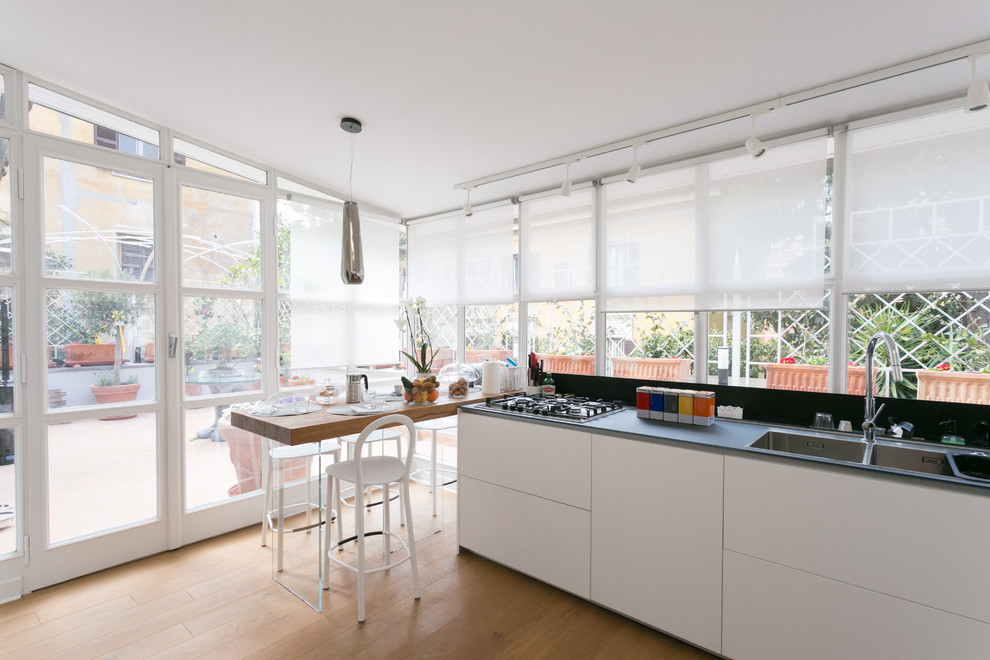 Moderne Wohnküche mit Doppelwaschbecken, flächenbündigen Schrankfronten, weißen Schränken, braunem Holzboden, braunem Boden und schwarzer Arbeitsplatte in Rom