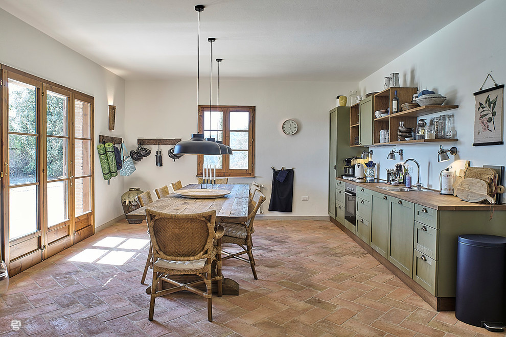 フィレンツェにある広いカントリー風のおしゃれなキッチン (レイズドパネル扉のキャビネット、緑のキャビネット、木材カウンター、白いキッチンパネル、シルバーの調理設備、レンガの床、アイランドなし、赤い床) の写真
