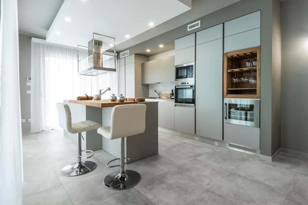 Inspiration for an eclectic galley porcelain tile and gray floor kitchen remodel in Bologna with flat-panel cabinets, gray cabinets, wood countertops, gray backsplash, paneled appliances, an island and brown countertops