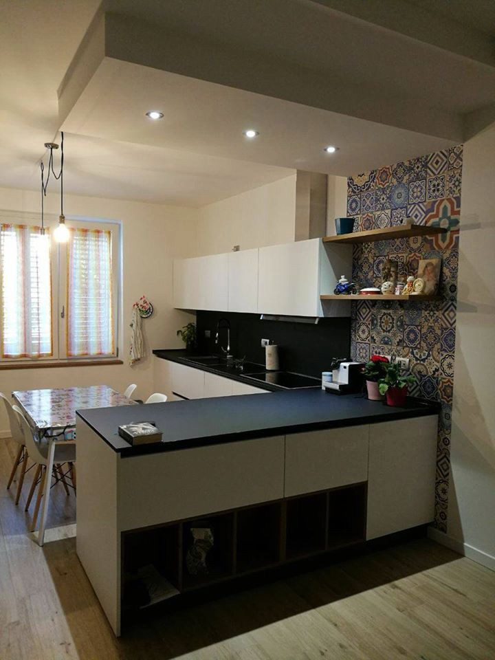 Medium sized contemporary l-shaped open plan kitchen in Milan with a built-in sink, flat-panel cabinets, white cabinets, laminate countertops, black splashback, stainless steel appliances, a breakfast bar and black worktops.