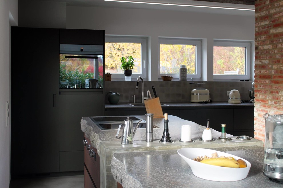 Moderne Wohnküche mit flächenbündigen Schrankfronten, dunklen Holzschränken, Mineralwerkstoff-Arbeitsplatte, Küchenrückwand in Grau, Kücheninsel, grauem Boden und grauer Arbeitsplatte in Stuttgart