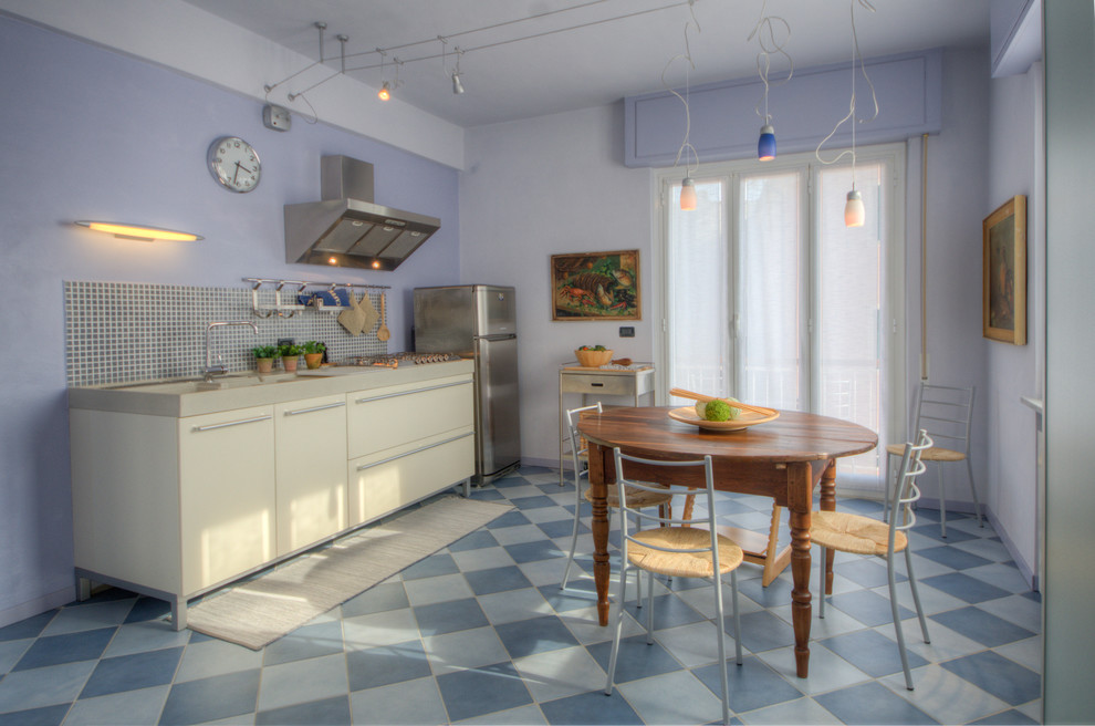 Exemple d'une petite cuisine américaine linéaire bord de mer avec un placard à porte plane, des portes de placard blanches, une crédence bleue, un électroménager en acier inoxydable, aucun îlot et un sol bleu.
