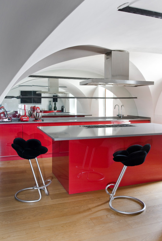Стильный дизайн: кухня в современном стиле с врезной мойкой, плоскими фасадами, красными фасадами, зеркальным фартуком, светлым паркетным полом, островом и серой столешницей - последний тренд