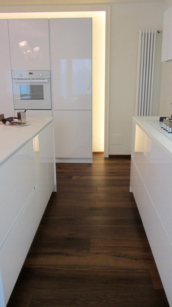 Zweizeilige, Mittelgroße Moderne Küche mit integriertem Waschbecken, flächenbündigen Schrankfronten, Mineralwerkstoff-Arbeitsplatte, weißen Elektrogeräten, dunklem Holzboden, Kücheninsel und weißer Arbeitsplatte in Sonstige