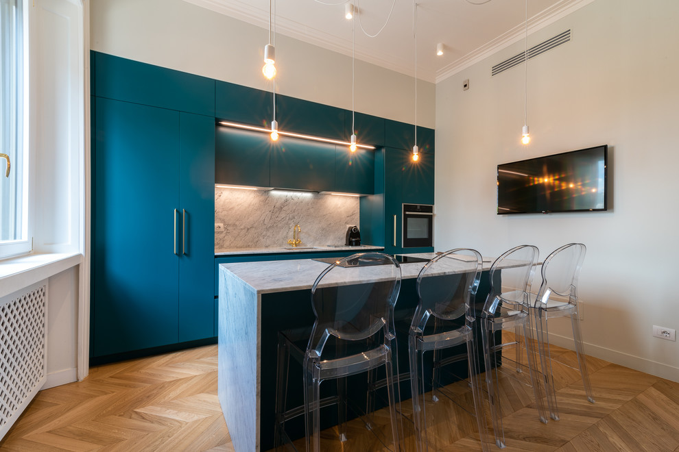 Cette image montre une cuisine parallèle design avec un placard à porte plane, des portes de placard bleues, une crédence blanche, un électroménager en acier inoxydable, îlot et un plan de travail blanc.