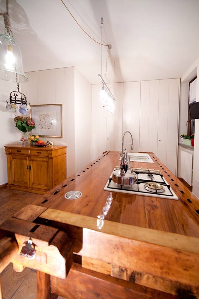 Lantlig inredning av ett litet kök, med en nedsänkt diskho, släta luckor, skåp i ljust trä, träbänkskiva, vita vitvaror, klinkergolv i terrakotta och en köksö