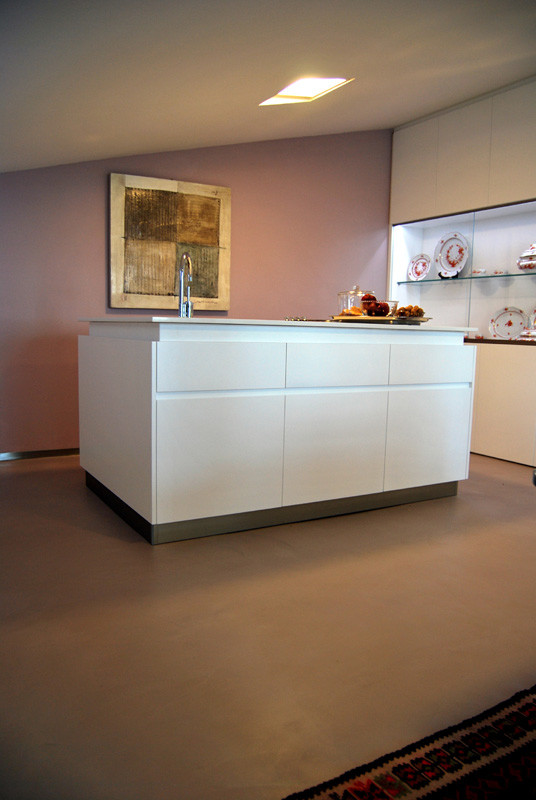 Inspiration pour une cuisine américaine parallèle et grise et rose minimaliste de taille moyenne avec un évier posé, un placard à porte plane, sol en béton ciré, îlot, un sol marron et un plan de travail blanc.