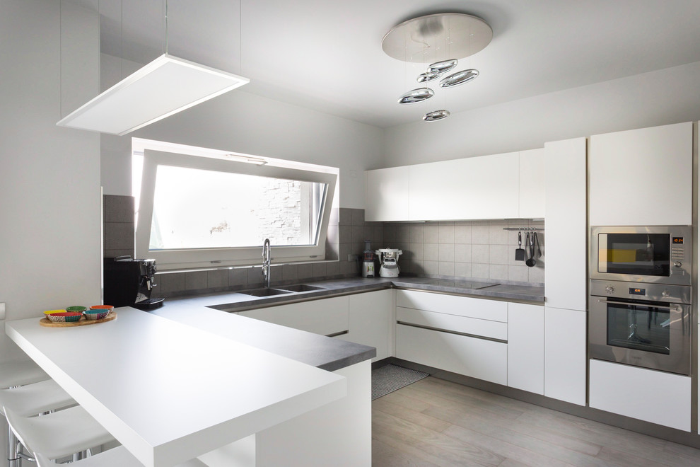 Exempel på ett modernt grå grått u-kök, med en dubbel diskho, släta luckor, vita skåp, grått stänkskydd, rostfria vitvaror, mörkt trägolv, en halv köksö och brunt golv